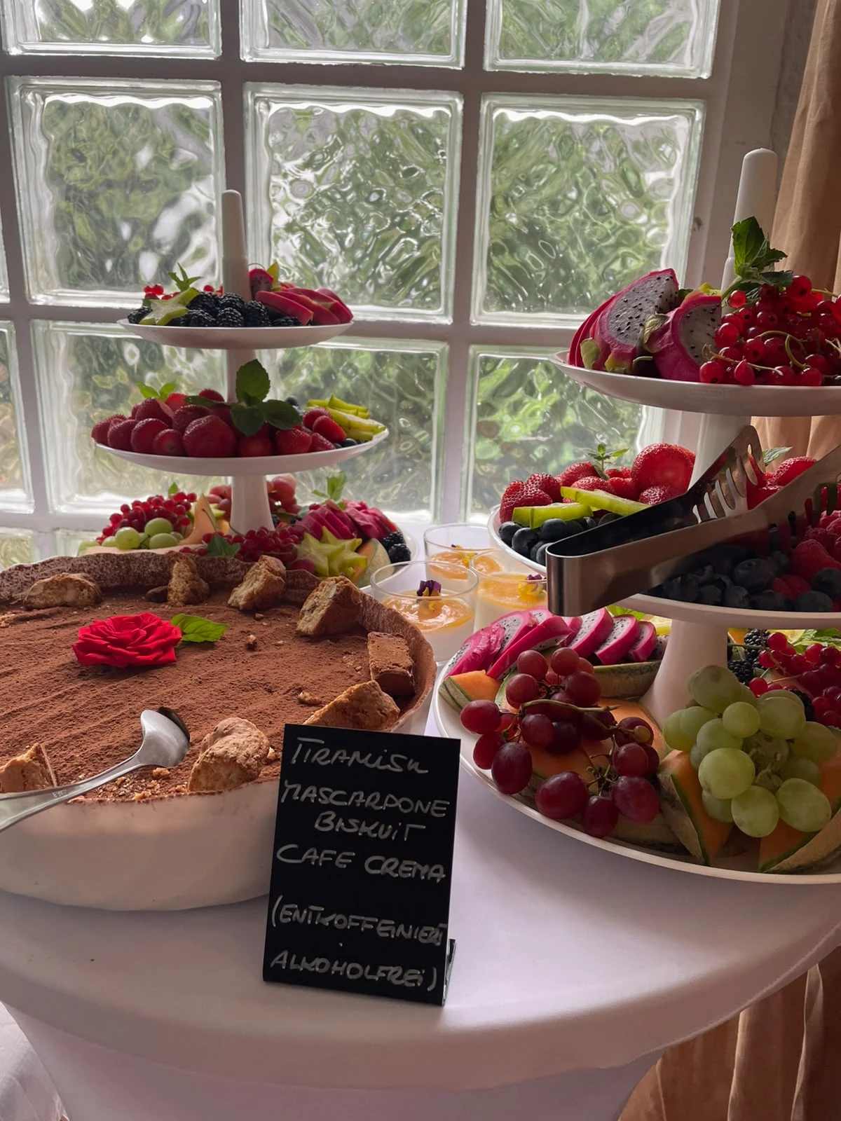 Buffet mit Etageren, Käse und Obst vor einem Fenster